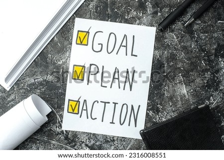 Above view of white sheet with GOAL PLAN ACTION writings ticks pens and notebook on black gray distressed background Royalty-Free Stock Photo #2316008551