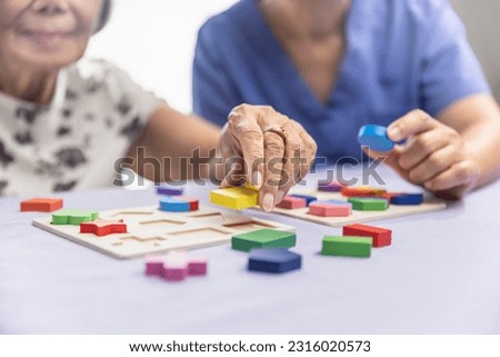 Caregiver and senior woman playing wooden shape puzzles game for dementia prevention Royalty-Free Stock Photo #2316020573