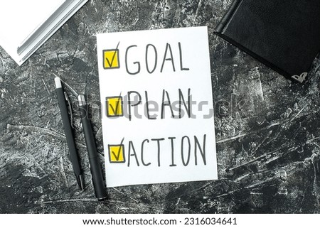 Top view of white sheet with GOAL PLAN ACTION writings ticks pens and notebook on black gray distressed background