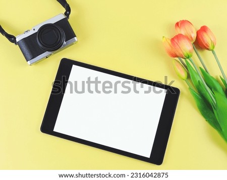 Top view or flat lay of digital tablet with blank white screen, tuip flowers  and digital camera isolated on yellow background.