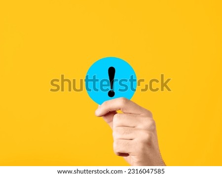 Attention and warning communication concept. Male hand showing a blue circle with exclamation mark symbol on yellow background.