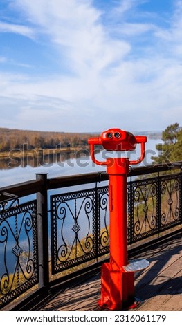 Public stationary binoculars on the banks of the river in summer or autumn to look at nature, coin-operated red metal binoculars. Royalty-Free Stock Photo #2316061179
