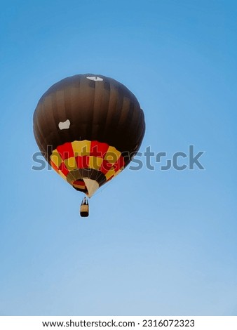 A big balloon of bright color is flying in the blue sky. Balloon in the sky. A big ball like from the cartoon "Up". Beautiful big bright balloon