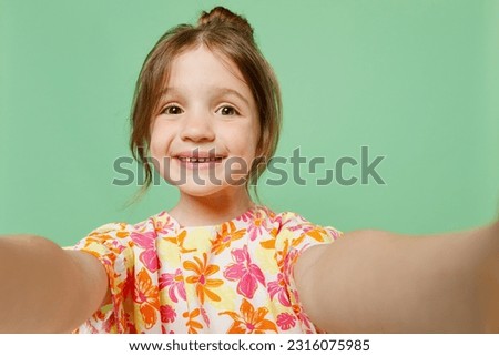 Close up smiling happy little child kid girl 6-7 years old wears casual clothes have fun do selfie shot pov on mobile cell phone isolated on plain green background. Mother's Day love family concept