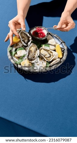 Vertical side view of a woman's hand picking up a fresh oyster, a luxury dining moment captured Royalty-Free Stock Photo #2316079087