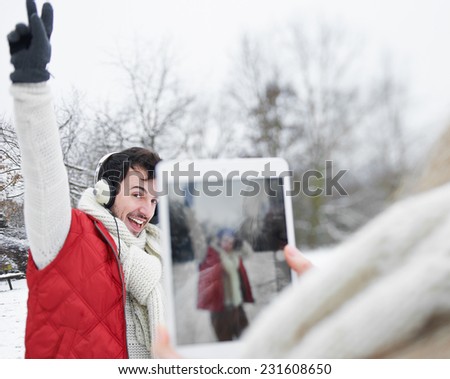 Woman taking pictures of man with headphones with tablet computer in winter