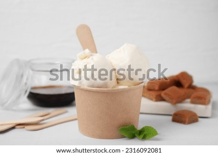 Delicious vanilla ice cream in paper cup on white wooden table