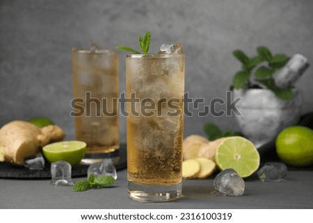 Glass of tasty ginger ale with ice cubes and ingredients on grey table Royalty-Free Stock Photo #2316100319