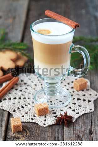 Hot coffee with milk in a glass on a old wooden table with pieces of sugar and cinnamon sticks. Selective focus