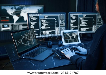 Information on screens. Young professional female hacker is indoors by computer with lot of information on displays.