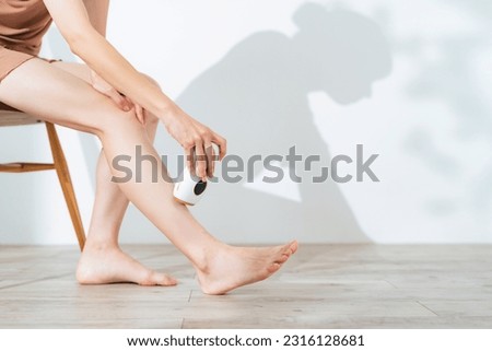 A woman using an epilator to remove unwanted leg hair at home. Royalty-Free Stock Photo #2316128681