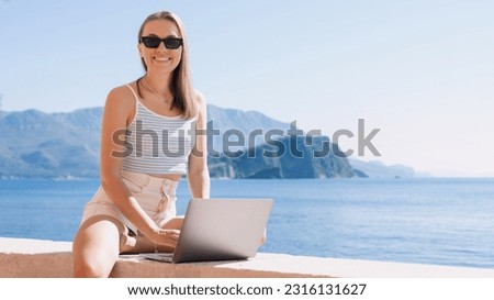 Young woman embraces the freelance lifestyle, effortlessly working on her laptop while appreciating the calming presence of the sea Royalty-Free Stock Photo #2316131627