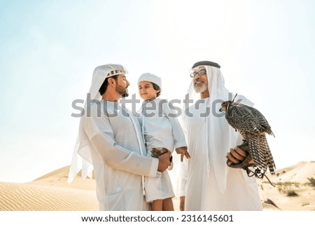 Three generation family making a safari in the desert of Dubai. Grandfather, son and grandson spending time together in the nature and training their falcon bird. Royalty-Free Stock Photo #2316145601