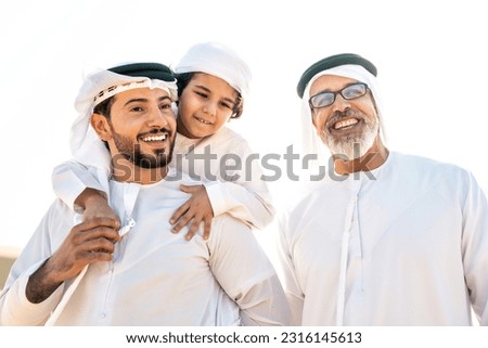 Three generation family making a safari in the desert of Dubai wearing white kandura outfit. Grandfather, son and grandson spending time together in the nature. Royalty-Free Stock Photo #2316145613