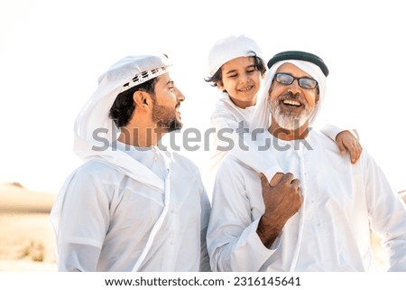 Three generation family making a safari in the desert of Dubai wearing white kandura outfit. Grandfather, son and grandson spending time together in the nature. Royalty-Free Stock Photo #2316145641