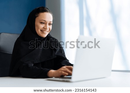 Beautiful woman with abaya dress working on her computer. Middle aged female employee at work in a business office in Dubai. Concept about middle eastern cultures and lifestyle Royalty-Free Stock Photo #2316154143