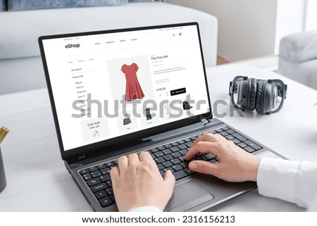 Woman purchasing a stunning red dress online with laptop computer. Modern ecommerce web page interface Royalty-Free Stock Photo #2316156213