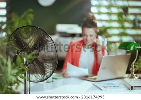 Sustainable workplace. Closeup on happy modern woman worker at work with electric fan and laptop. Royalty-Free Stock Photo #2316174995