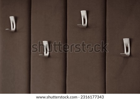 A soft wall upholstered with a furry brown fabric with silver hooks for clothes close-up with a blurred background. Hanger on a striped velour surface with fittings for hanging outerwear. Royalty-Free Stock Photo #2316177343