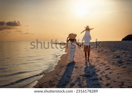 A elegant family in white clothing walks hand in hand down a tropical paradise beach during sunset tme and enjoys their summer vacatios Royalty-Free Stock Photo #2316178289