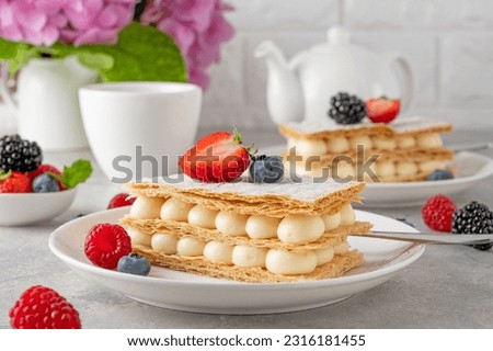 Traditional French dessert millefeuille with vanilla cream and fresh berries on a white plate on a gray concrete background