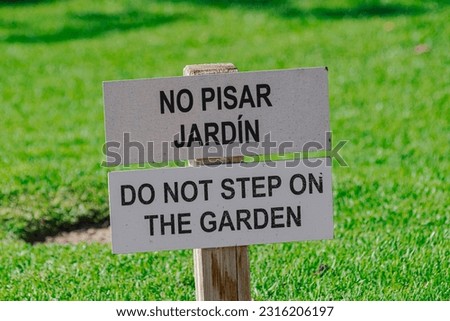 Do no step on the garden sign, in english and spanish, with green grass background
