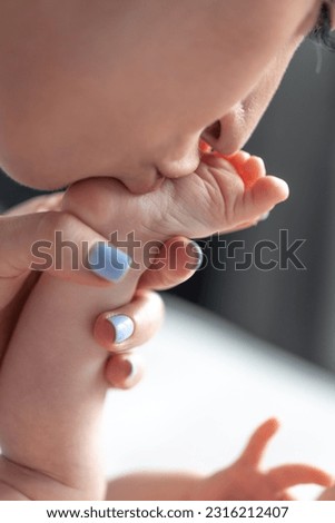 Close portrait of adorable young mother kissing baby's feet with tiny toes.