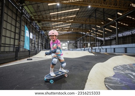 asian child skater or kid girl fun playing skateboard or smile ride surf skate in indoor pump track in skate park by extreme sports surfing to wears helmet elbow pads wrist knee guard for body safety Royalty-Free Stock Photo #2316215333
