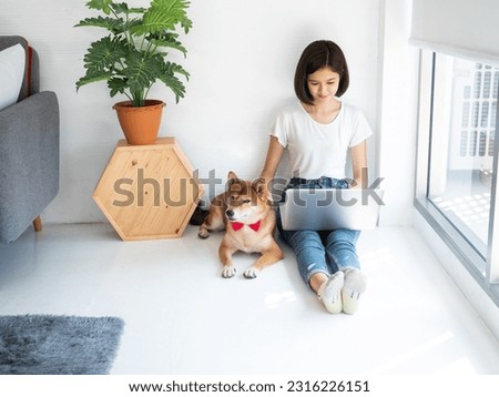Asian young freelance girl productive work at home lifestyle while using computer device with smart handsome dog pet lie down on the floor in living room
