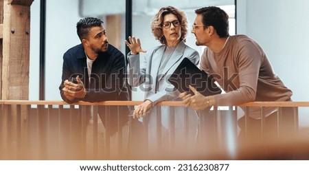 Interior designers discuss with each other in an office. Three business people talking while standing on an interior balcony. Group of creative business people work as a team on a project. Royalty-Free Stock Photo #2316230877