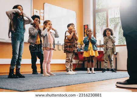 School children moving along to an educational song, kids participating in a class activity with their teacher. Boys and girls stand together and follow their teacher's instruction in a classroom. Royalty-Free Stock Photo #2316230881