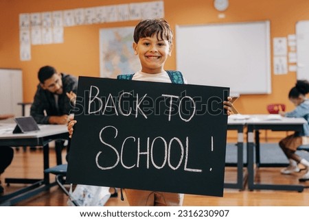 Excited child ready for first day of co-ed schooling and lifelong learning. Happy young boy standing in a classroom with a back to school sign. Elementary school kid starting a new class.
