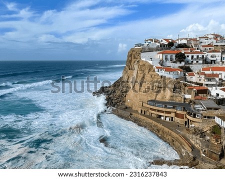 The picture shows the small village of Azenhas do Mar, nestled on the cliffs of the Atlantic Ocean near Lisbon in Portugal. You can see powerful waves breaking on the cliffs on a windy day.