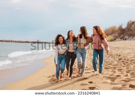 Multiracial group of four young women reunited walking and laughing on an empty beach