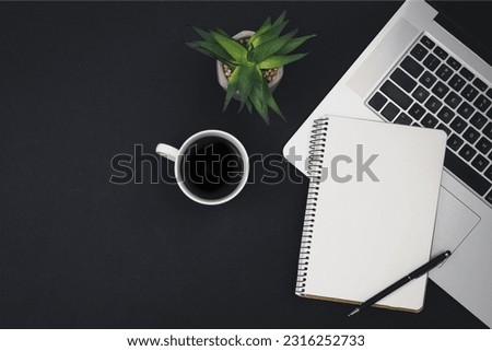 Laptop, coffee cup and notepad on black background, top view.