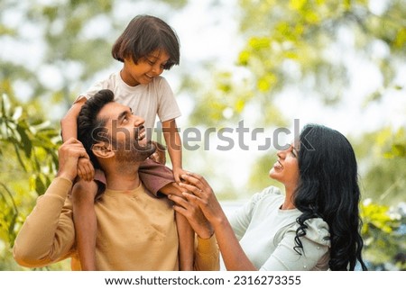 Happy indian parents playing with daughter while kid on father shoulder at outdoor - concept of parenthood, family bonding and weekend holidays Royalty-Free Stock Photo #2316273355
