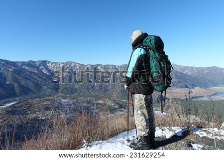 The man with a backpack standing on mountain top looking at a mountain landscape in the fall