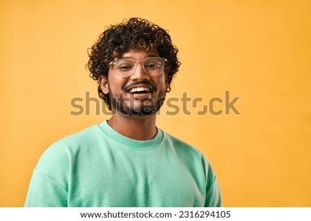 Close-up portrait of a handsome curly-haired Indian man in a turquoise t-shirt and glasses laughing and looking at the camera.