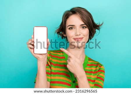 Photo of cheerful cute woman dressed striped t-shirt pointing finger gadget empty space isolated turquoise color background