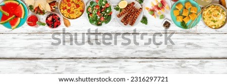 Summer food top border over a white wood banner background. Selection of refreshing salads, fruit, wraps and BBQ grilled skewers. Overhead view. Copy space.