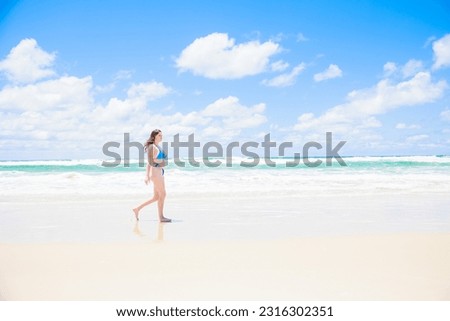 Caucasian woman in bikini walking in front of blue sky and sea