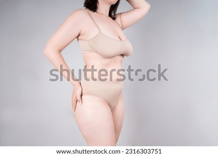 Fat woman in beige underwear on gray background, overweight female, body positive concept