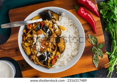 Vegan Roasted Eggplant and Chickpea Curry Served Over Rice: Aubergine curry served over a bowl of white rice and topped with plant-based cream Royalty-Free Stock Photo #2316317489