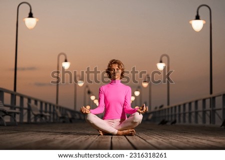 Young girl practices yoga and looking for peace and balance during meditation in solitude on wooden quay near seashore