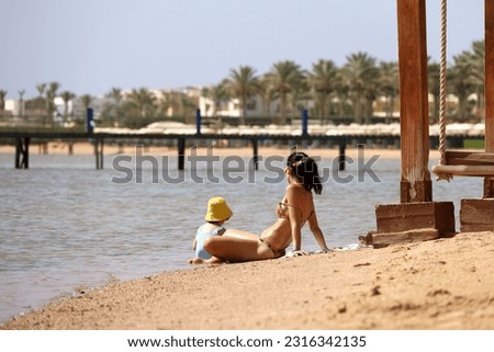 Young mother tanning with child on sea coast. Slim woman in bikini on a sandy beach