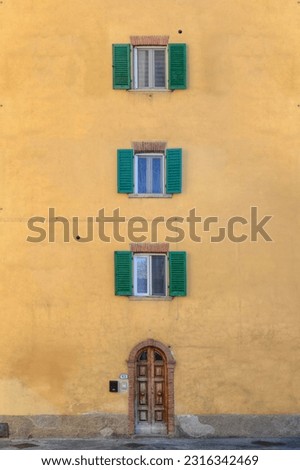 A frontal photo of a yellow building in Toscana Italy with a straight line of windows 