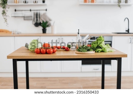 Wooden table filled with red and green organic components of healthy balanced diet on kitchen background. Common raw vegetables and greens for delicious homemade breakfast being ready for cooking. Royalty-Free Stock Photo #2316350433