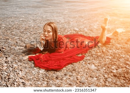 Woman travel sea. Happy tourist in red dress enjoy taking picture outdoors for memories. Woman traveler posing in sea beach, surrounded by volcanic mountains, sharing travel adventure journey