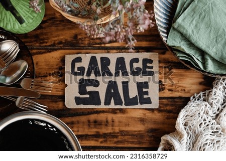 Garage sale sign and used items on wooden table.