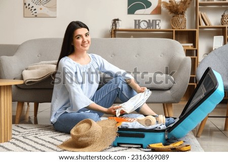 Young woman packing clothes in suitcase at home Royalty-Free Stock Photo #2316369089